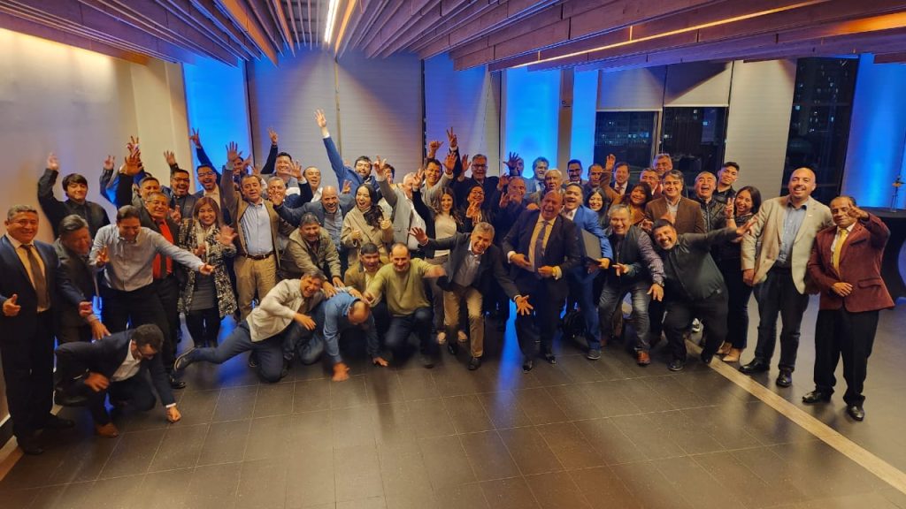 Un gran grupo de personas celebrando en un evento social en un salón moderno con iluminación azul. Los asistentes, de diversas edades, están sonrientes y levantando las manos, mostrando alegría y entusiasmo. La imagen captura una atmósfera de camaradería y felicidad compartida, resaltando la energía positiva del momento. Ideal para artículos sobre eventos sociales, reuniones de equipo y celebraciones.